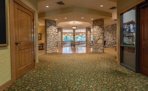 A spacious lobby with a patterned carpet, stone pillars, and a view of the dining area.