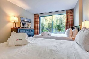 A hotel room with two beds, a TV, a desk, and a window with curtains.