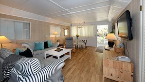 A modern living room with striped sofas, a white coffee table, and a television mounted on the wall. - 334S: Quaint Catalina Cottage, Large Porch, BBQ, WIFI, Min Away from Beach - 334 (Avalon)