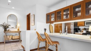 Une cuisine moderne avec des meubles en bois, un plan de travail blanc et deux tabourets de bar en osier.