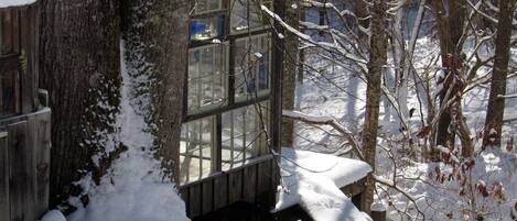 A wooden cabin with a glass window, surrounded by snow-covered trees.