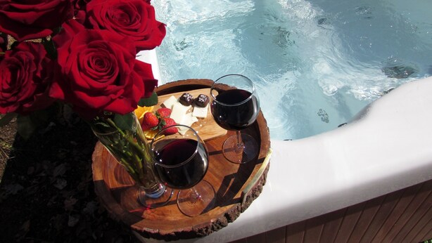 Un bain à remous décoré de roses et agrémenté de verres à vin posés sur un plateau en bois.