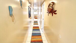 Un pasillo con un colorido tapete a rayas, una gran decoración de escorpión en la pared y una obra abstracta azul y blanca en la pared izquierda.