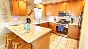 Una cocina moderna con gabinetes de madera, estufa de acero inoxidable, microondas y un lavamanos. Hay taburetes en la isla y una cafetera en la encimera.