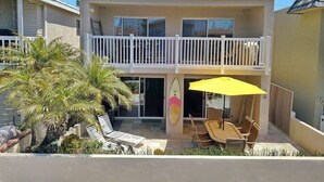 Un edificio de dos pisos con un balcón, una decoración con una tabla de surf y mobiliario exterior.