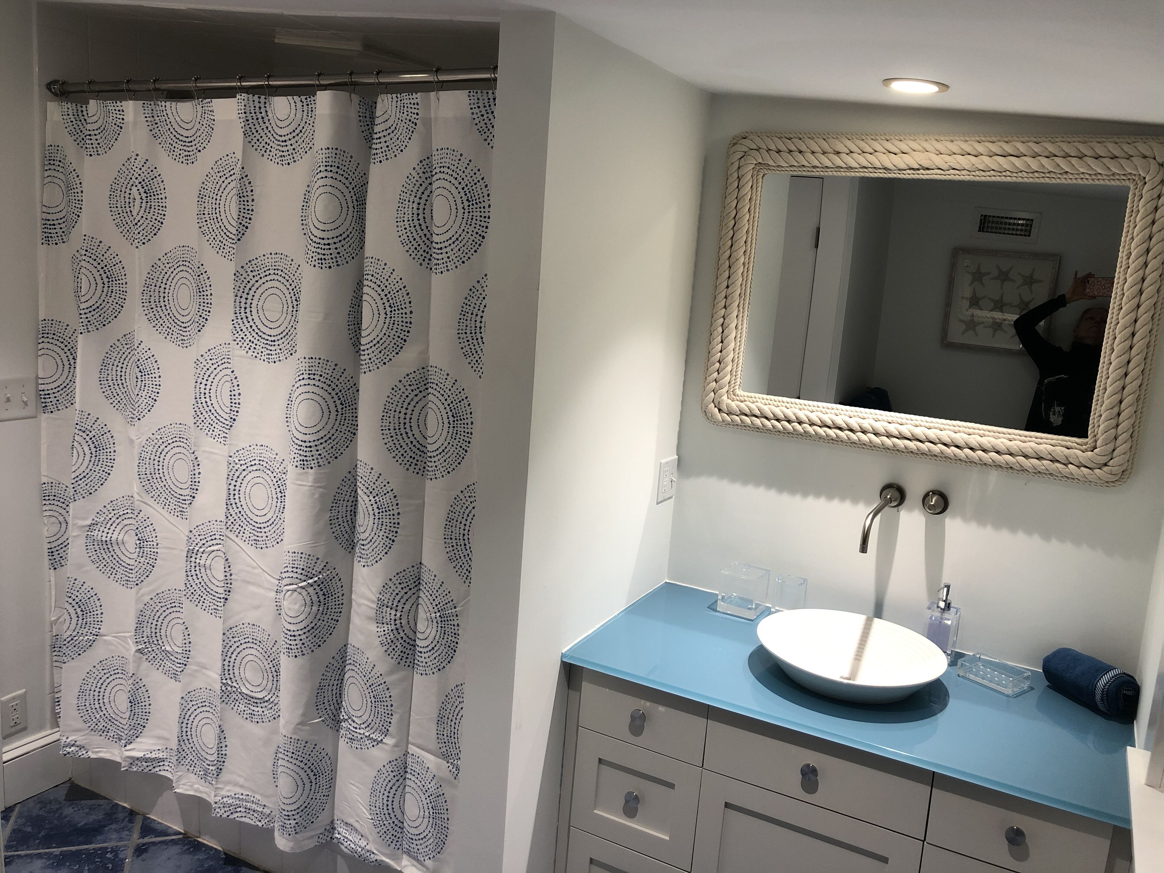 A bathroom with a blue countertop, a white sink, and a mirror with a rope frame.