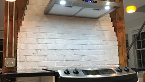 Eine Küche mit weißer Ziegelwand, einer Edelstahl-Dunstabzugshaube und einem schwarzen Backofen, versehen mit einem gestreiften Handtuch.