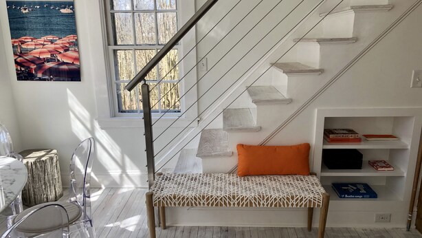 Ein modernes Zimmer mit einer Holzbank, klaren Stühlen, einer Treppe und Blick auf Boote durch ein Fenster.