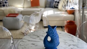 Ein Wohnzimmer mit einem weißen Sofa, klaren Plastikstühlen und einem Marmortisch mit einer blauen Vase.