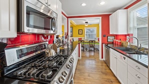 A modern kitchen with stainless steel appliances, a wooden floor, and a bright yellow accent wall. - 315E Upper: Spacious, Remodeled, Colorful Upper Level Duplex, Quiet Street, WIFI (Avalon)