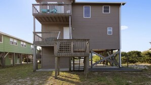 A two-story building with a balcony on the upper floor and a wooden deck in front. - Discover ocean views at Moonlighting, a spacious 4-bedroom home in Topsail Beach! (Topsail Beach)