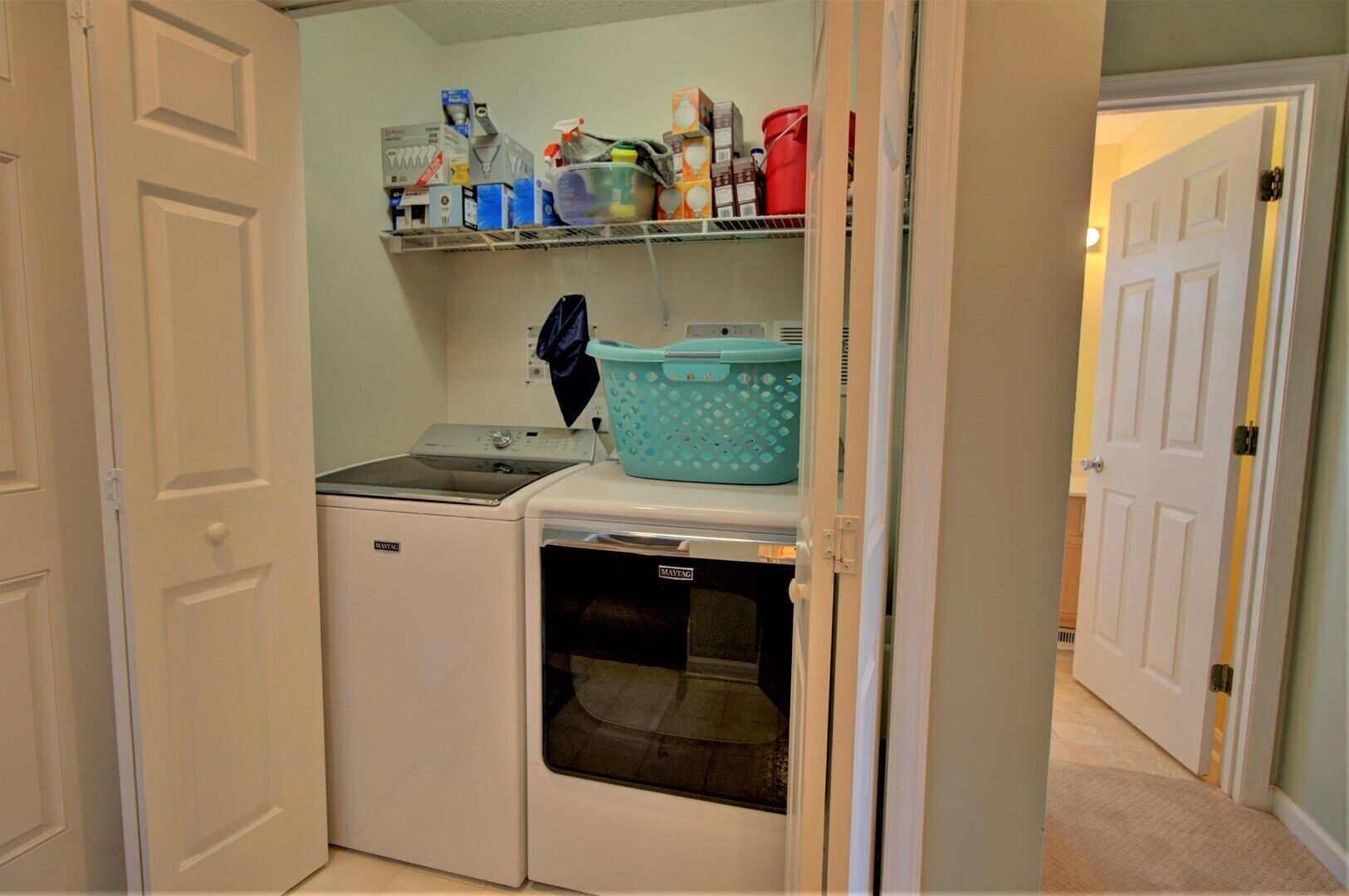 A laundry room with a washing machine and dryer, a shelf with cleaning supplies, and a basket.