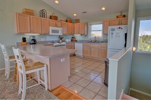 A modern kitchen with wooden cabinets, a central island, a microwave, a stove, and a refrigerator. - Discover ocean views at Moonlighting, a spacious 4-bedroom home in Topsail Beach! (Topsail Beach)