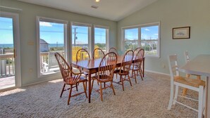 A dining area with a large table and chairs, large windows, and a view of the outdoors. - Discover ocean views at Moonlighting, a spacious 4-bedroom home in Topsail Beach! (Topsail Beach)