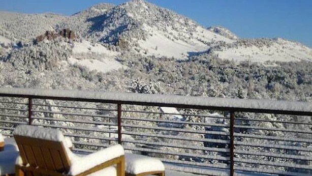 Un paisaje nevado de montañas con una terraza de madera y dos sillas.