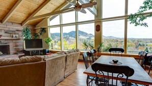 Un amplio salón con un gran ventanal que ofrece vistas a la montaña, una chimenea y una zona de comedor con mesa y sillas.