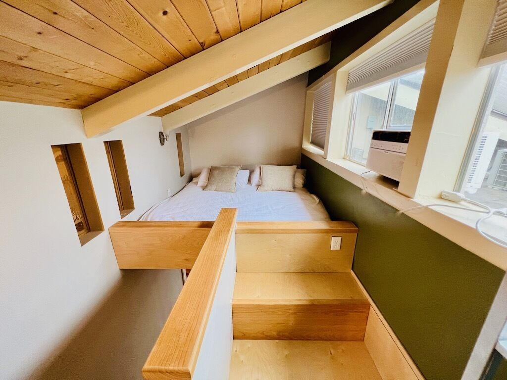 A bedroom with a wooden bunk bed, a window with blinds, and a small desk area.
