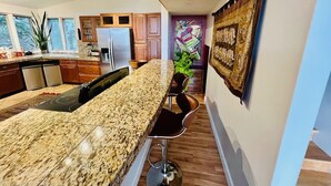 Una cocina moderna con encimeras de granito, refrigerador de acero inoxidable, gabinetes de madera y una zona de bar con taburetes.