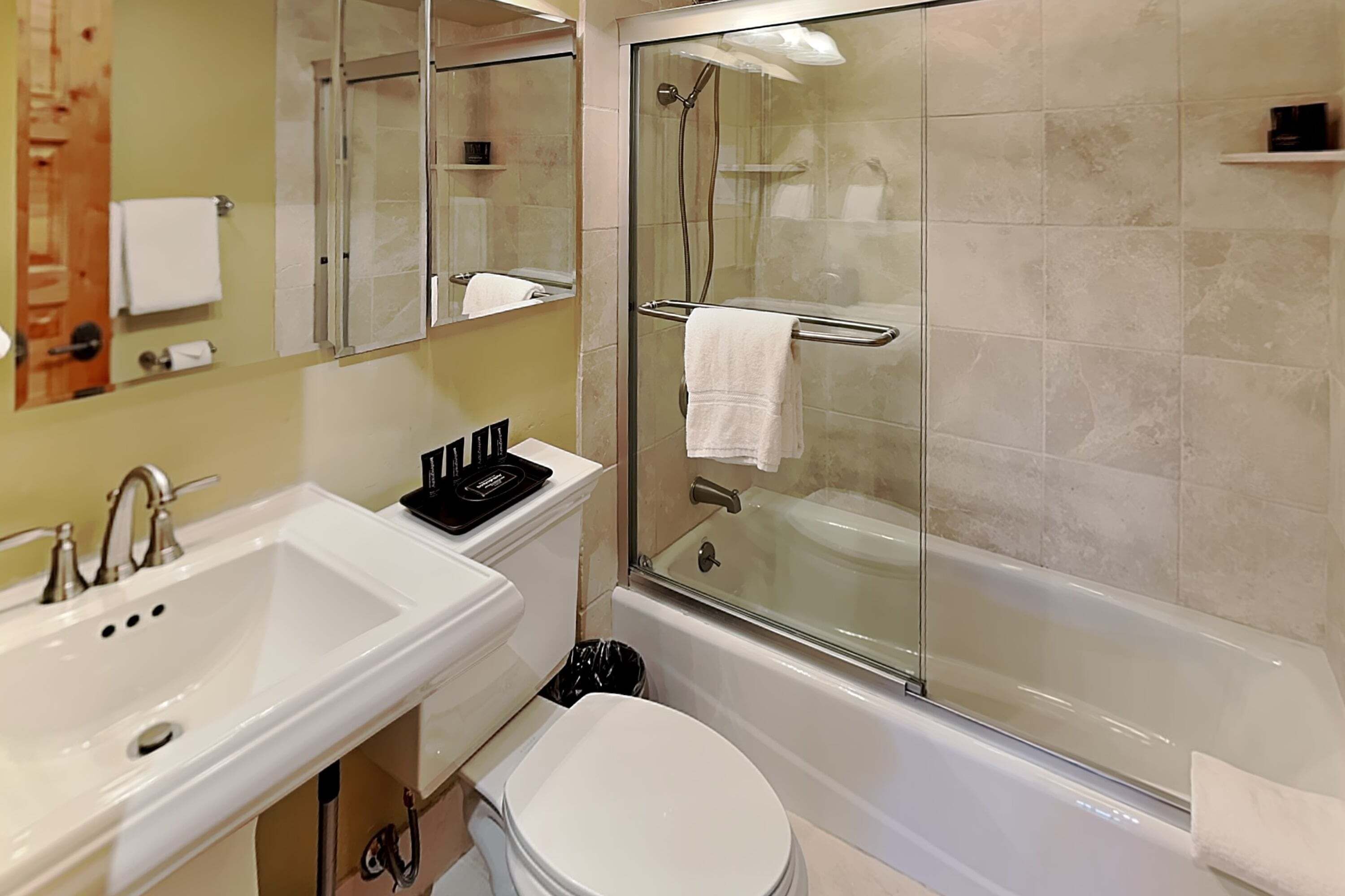 A bathroom with a white sink, mirror, toilet, and glass-enclosed shower area.