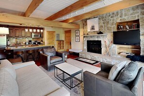 A spacious living area with a fireplace, stone wall, and a kitchen with wooden cabinets and bar stools.