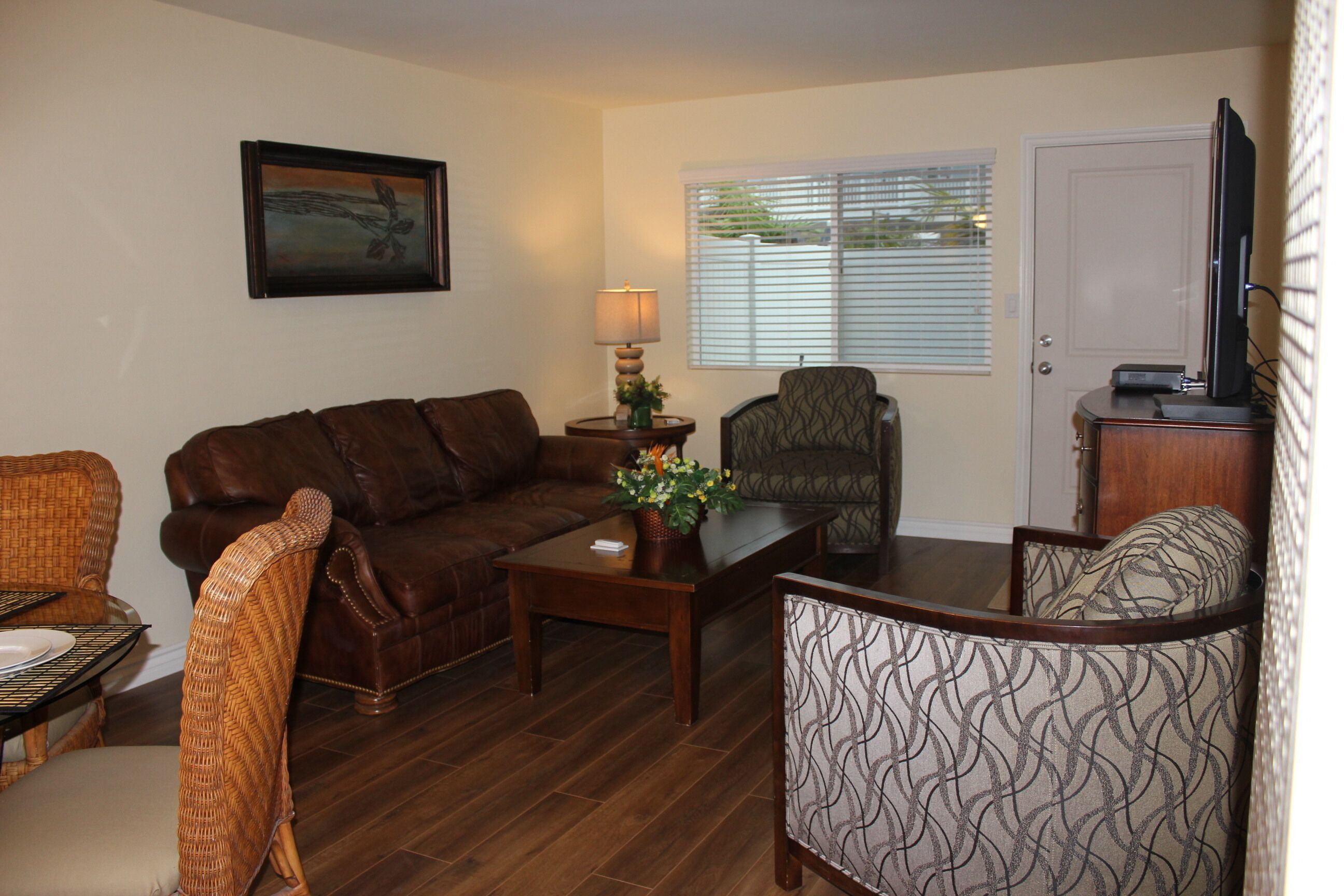 A living room with a brown leather sofa, a patterned armchair, a wooden coffee table, and a television on a wooden cabinet.