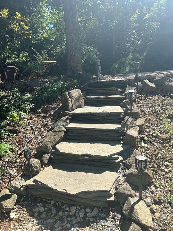 A stone pathway leading through a wooded area with steps and lanterns.