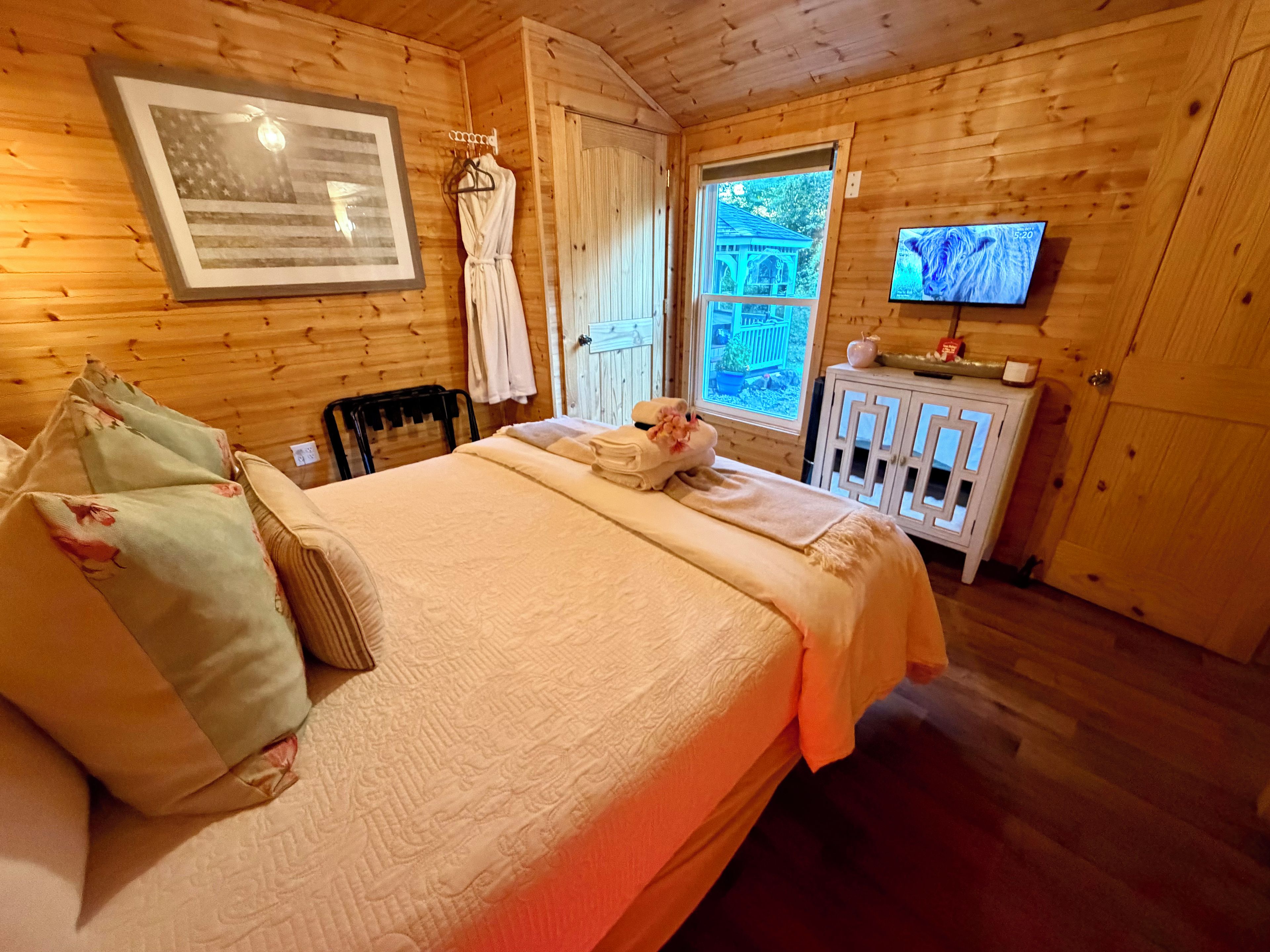 Une chambre dans un chalet en bois, équipée d’un lit, d’une télévision et d’une fenêtre donnant sur un paysage verdoyant.