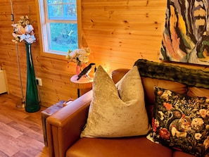 A wooden interior with a sofa, a green vase with flowers, and a painting on the wall. - Apple Blossom Cottage Of Gettysburg.  Hot Tub is an Add on Fee (Orrtanna)