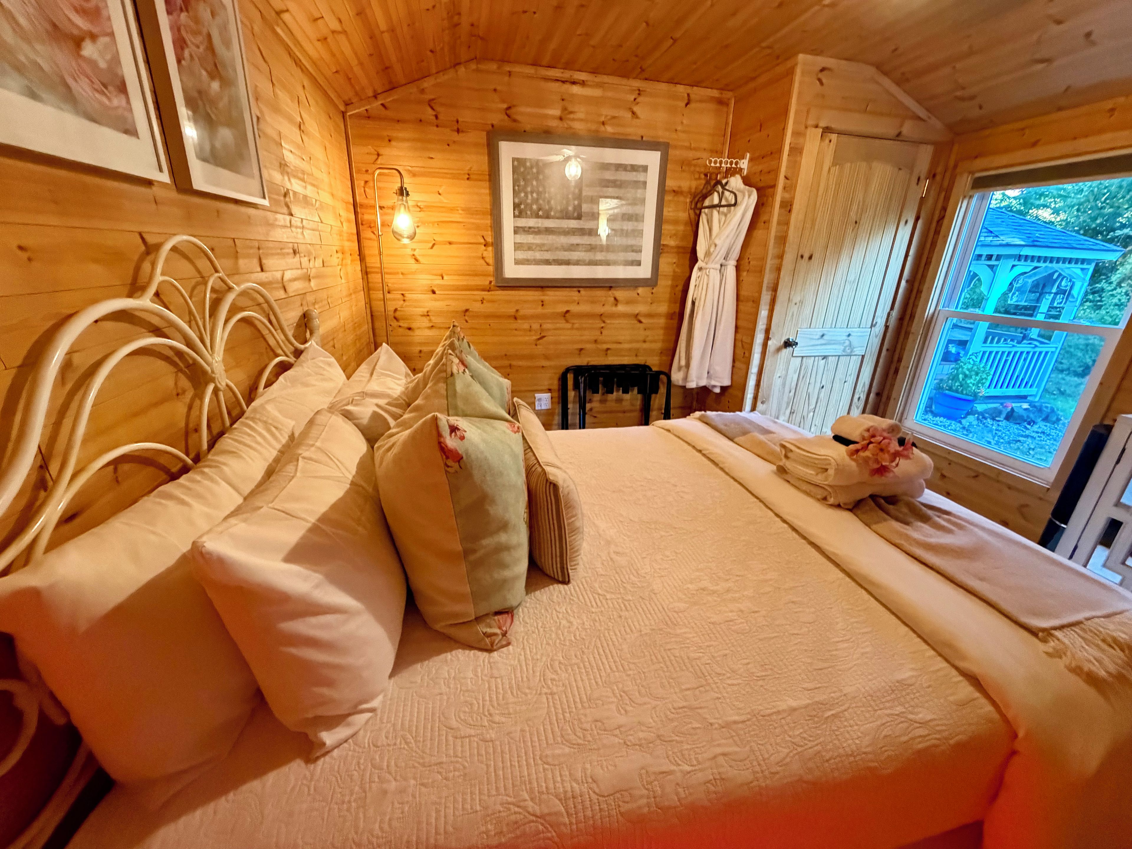 A wooden room with a bed, a framed picture, a light fixture, and a window.
