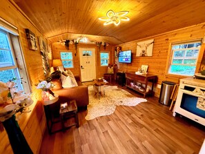 Interior acolhedor de uma cabana, com decoração em madeira, televisão, lareira e uma janela grande.
