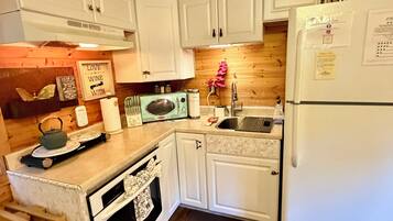 Una cocina con gabinetes blancos, techo de madera, refrigerador, microondas y un lavamanos.