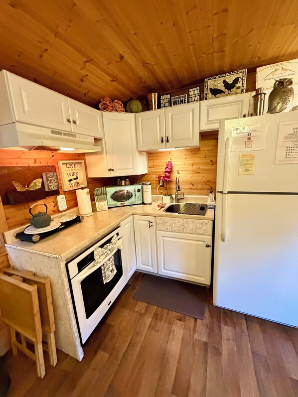 A kitchen with white cabinets, a wooden ceiling, a refrigerator, a microwave, and a sink.