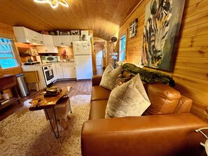 A cozy interior with a brown leather sofa, a wooden dining table, and a kitchen area with white cabinets and a refrigerator. - Apple Blossom Cottage Of Gettysburg.  Hot Tub is an Add on Fee (Orrtanna)