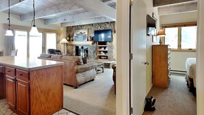 A spacious living area with a stone fireplace, a television, and a large window. - 🌲Timberline D2E Deluxe 3-Bedroom ~Hot Tub~Pool~WiFi~Ski-in/out~Local Shuttle🌲 (Snowmass Village)