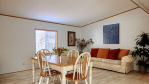 A dining area with a wooden table and chairs, a sofa with orange cushions, and a large painting on the wall. - Bear Creek Ranch in tranquil setting near Yosemite Valley/Merced River (Catheys Valley)