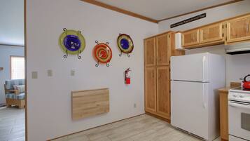 A kitchen with wooden cabinets, a white refrigerator, and a stove. There are decorative plates on the wall and a fire extinguisher.