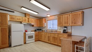 A kitchen with wooden cabinets, a refrigerator, stove, microwave, and a small dining area with a chair. - Bear Creek Ranch in tranquil setting near Yosemite Valley/Merced River (Catheys Valley)