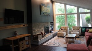 A living room with a stone fireplace, large windows, and a television mounted on the wall. - FOOTBALL WEEKEND GET-A-WAY - with outdoor space to die for. (South Bend)