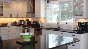 A modern kitchen with white cabinets, a large island, and a window with a view of trees. - FOOTBALL WEEKEND GET-A-WAY - with outdoor space to die for. (South Bend)