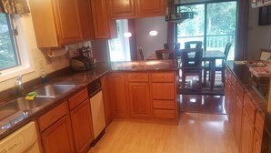 Una cocina con armarios de madera, lavavajillas, fregadero y comedor con sillas y mesa.