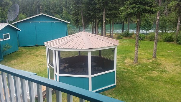 Una pérgola con techo metálico y paredes de vidrio, rodeada por una terraza con barandilla.