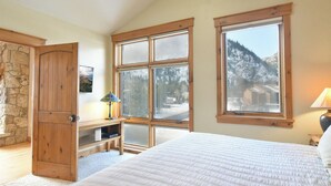 Een slaapkamer met een groot bed, een houten garderobe, een bureau met een lamp en uitzicht op besneeuwde bergen door een raam.