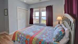 A bedroom with a bed, a ceiling fan, a window with curtains, and a view of the sea. - Surf Monkeys: A stunning 5-bedroom oceanfront home in Surf City, NC. (Surf City)