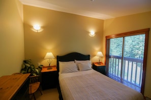 Quarto com cama, duas luminárias de cabeceira, mesa de cabeceira de madeira, uma cadeira e janela com persianas.