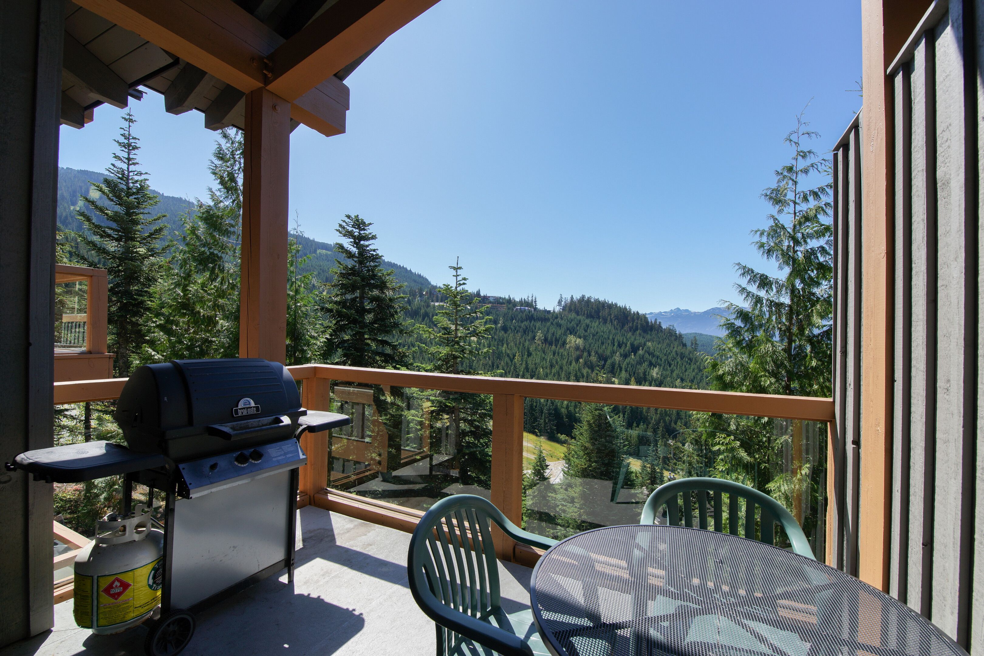 Un balcon équipé d’un barbecue, de chaises et offrant une vue panoramique sur les montagnes.