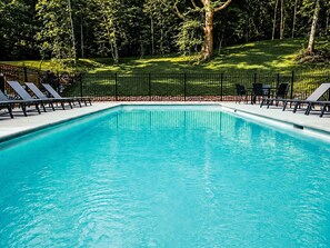 Una piscina rettangolare con recinzione in metallo nero e lettini intorno.