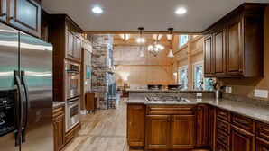 A spacious kitchen with wooden cabinets, a stainless steel refrigerator, a stone accent wall, and a central island with seating.