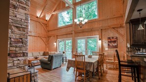 A spacious wooden cabin interior with a dining area, a stone accent wall, and large windows.