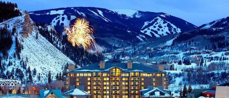 A hotel with multiple floors, a prominent building in the center, and snow-covered mountains in the background.