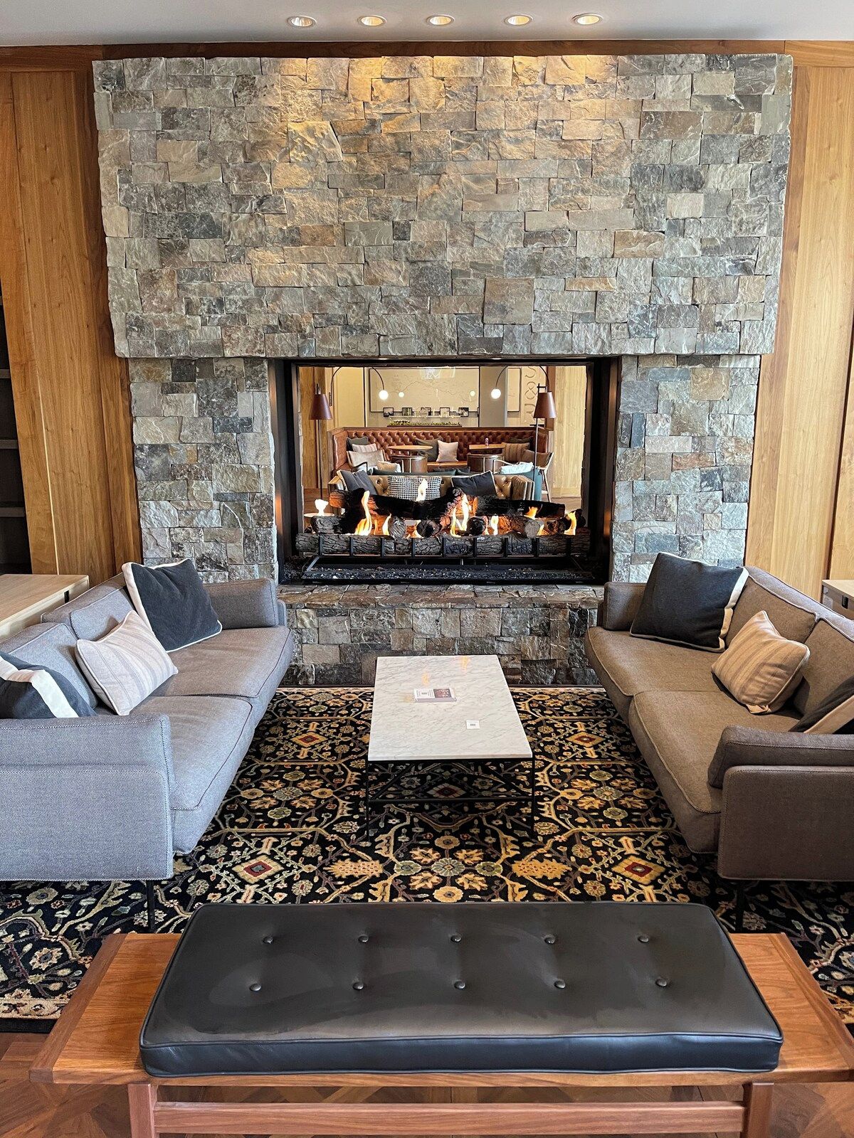 Un salon avec une cheminée en pierre, deux canapés, une table basse et un tapis à motifs.